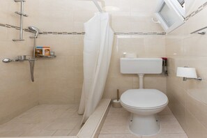 Ein Badezimmer mit Dusche, Toilette und einem kleinen Ablagebereich für Toilettenartikel.