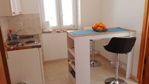 Une cuisine de taille réduite, dotée d’une fenêtre, d’un évier, d’un petit plan de travail et d’une chaise.