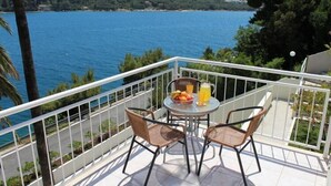 A balcony with two wicker chairs and a small table, overlooking a body of water with hills in the background. - Apartments Lozica - Standard Studio  Apartment with Terrace and Sea View (Mokosica)