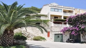 Un edificio de dos pisos con un balcón, un muro de piedra y una palmera.