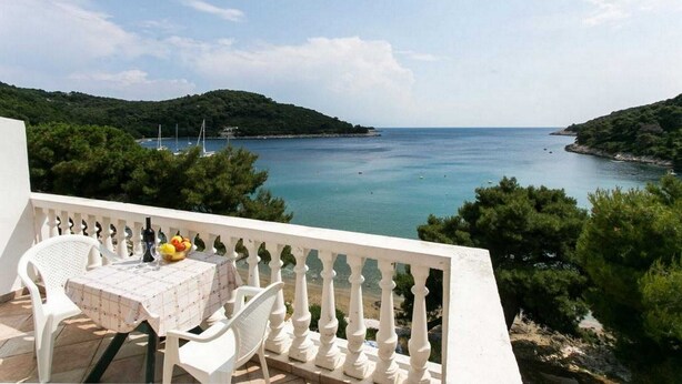 A balcony with a table set for two, overlooking a coastal bay with boats and greenery. - Apartments Franka Saplunara-One-Bedroom Apartment with Terrace and Sea View No1 (Saplunara)