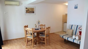 Un área de comedor con una mesa y sillas de madera, un sofá con cojines estampados y un aire acondicionado fijado a la pared.