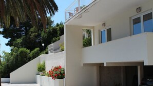 Un edificio moderno de dos pisos con balcón, cochera y jardín con flores rojas.