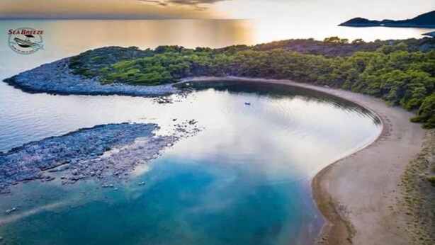 Vista aérea de una zona costera con playa arenosa, agua tranquila y vegetación verde exuberante.