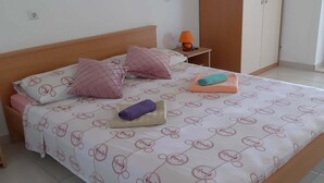 Una cama bien tendida con ropa de cama estampada, una mesita de noche con una lámpara y un armario al fondo.