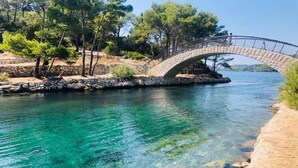 Un puente de piedra sobre un río azul cristalino, con árboles y una orilla rocosa.