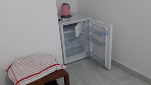 Una cocina pequeña con un refrigerador, un hervidor rosa y una mesa con mantel a cuadros.