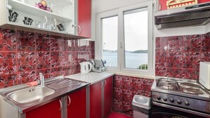 A kitchen with red cabinets, a stainless steel sink, a stove, and a window overlooking a body of water.