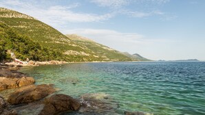 A coastal landscape with clear waters, rocky shore, and a hilly backdrop.
