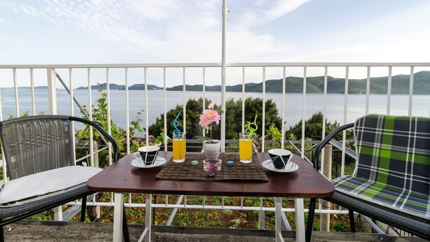 A balcony with a table, chairs, and a view of a lake and hills.