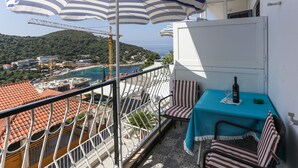 A balcony with a view of a coastal town, a table with a bottle and glasses, and striped chairs. - Lapad View Apartments - Studio Apartment with Balcony and Sea View (Dubrovnik)