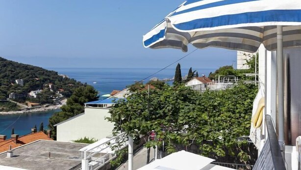 A coastal view with a blue and white striped umbrella, a clear sky, and a distant shoreline with buildings and greenery. - Lapad View Apartments - Studio Apartment with Balcony and Sea View (Dubrovnik)