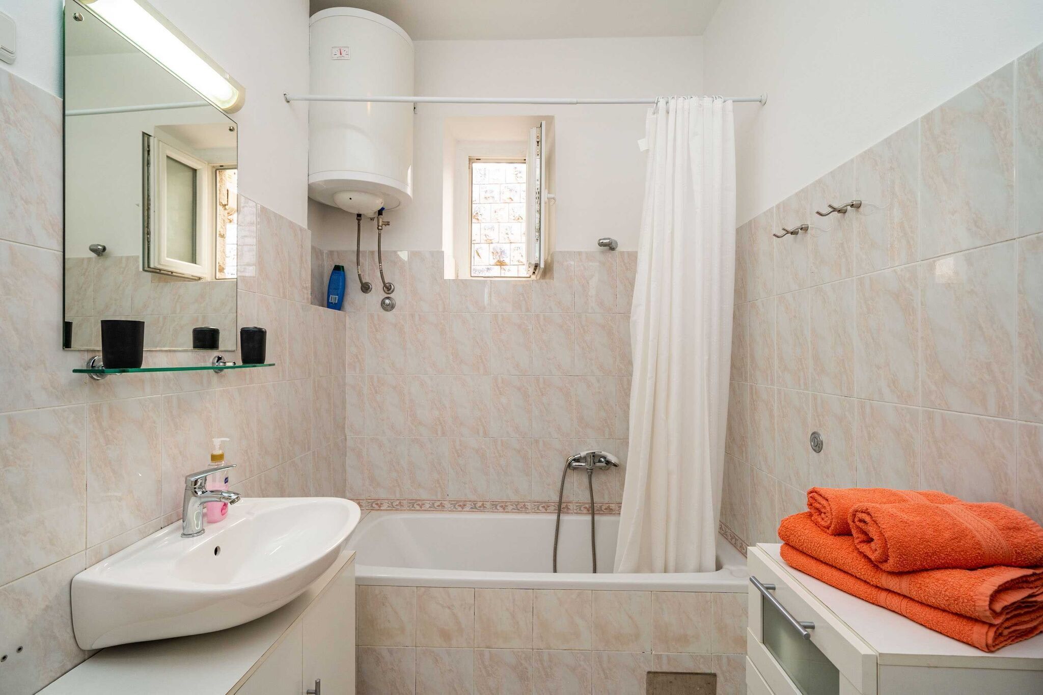 A bathroom with a sink, mirror, shower, and a towel rack.