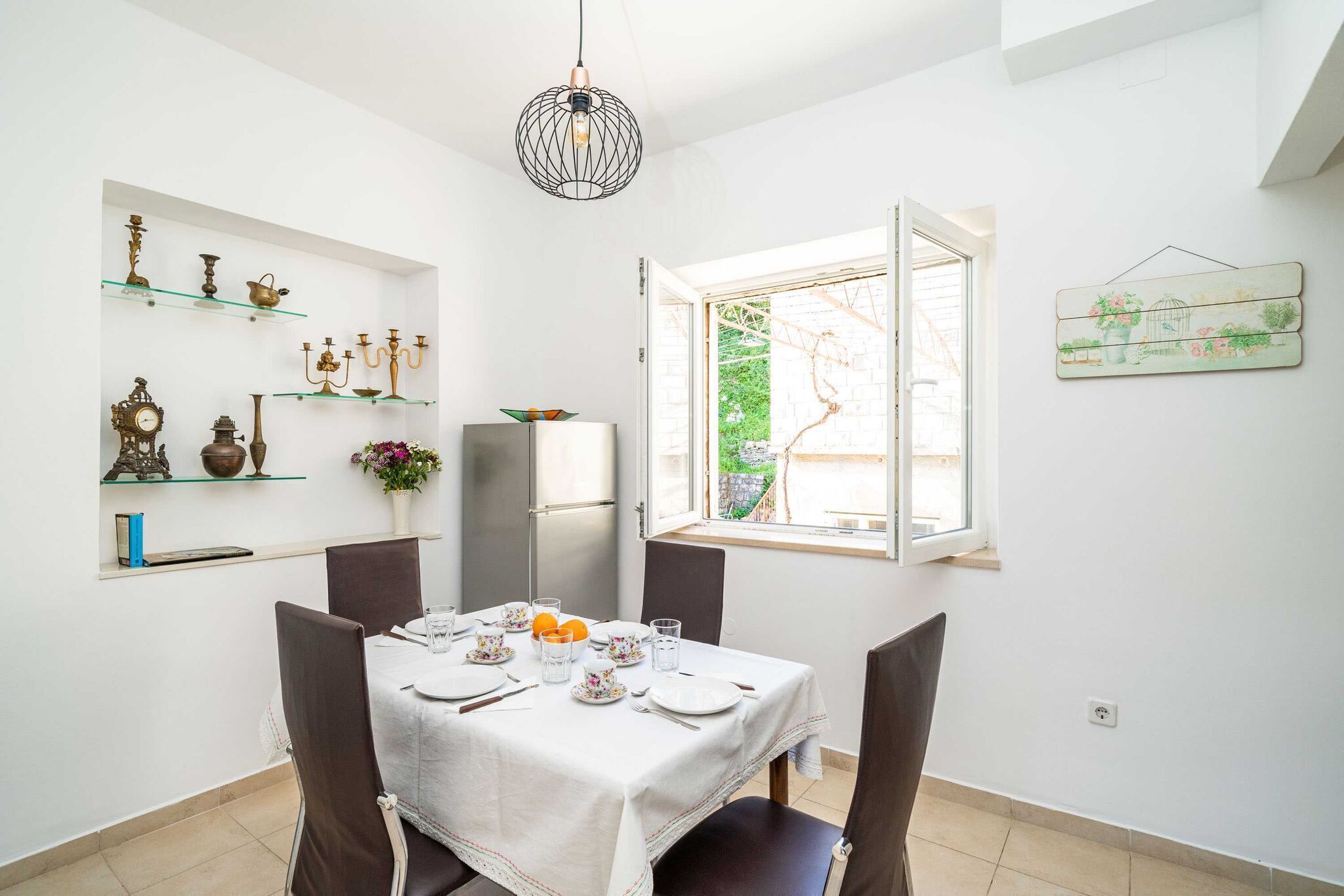 A dining area with a table set for four, a refrigerator, and decorative items on shelves.