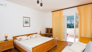 A bedroom with a wooden bed, a nightstand, a bedside table with a lamp, a framed picture on the wall, and a view through a sliding door. - Guest House Ljubica - Double Room with Private Bathroom-2 (Dubrovnik)