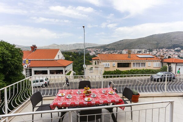 A terrace with a table set for dining, overlooking a residential area with red-roofed houses and a hilly landscape.
