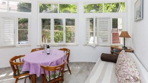 A room with a dining table, chairs, a sofa, and large windows with shutters.