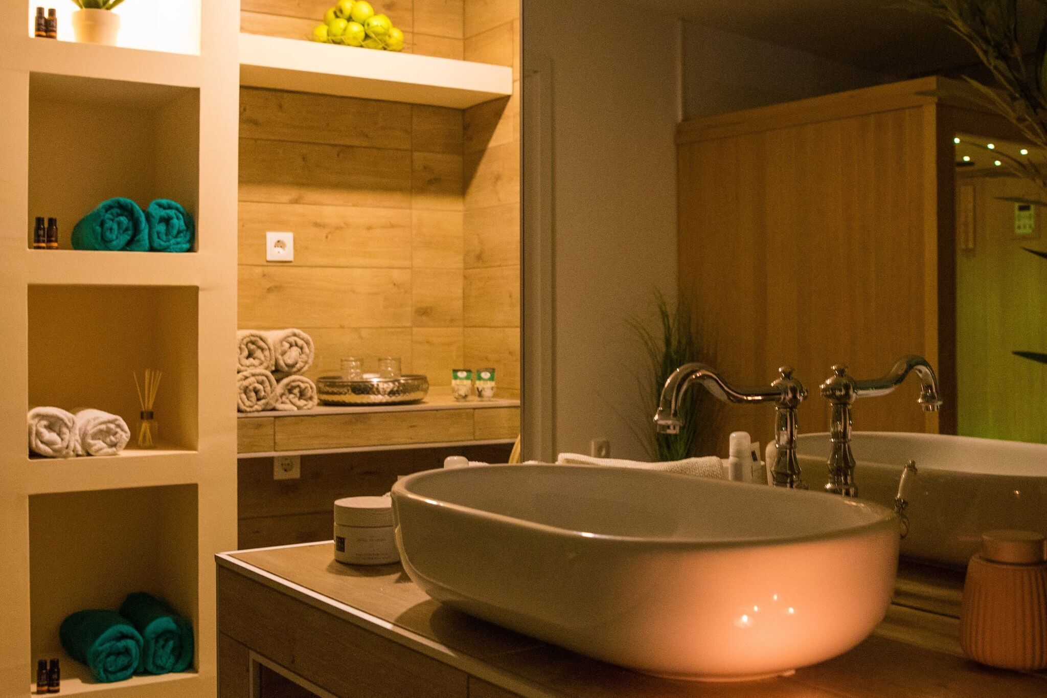 Een badkamer met een groot ovaal wastafel, een spiegel en planken met handdoeken en toiletartikelen.