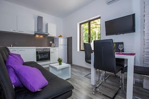 Enjoy a compact living space with a kitchenette, sofa, dining area, and flat-screen TV, offering a view of the surrounding greenery.