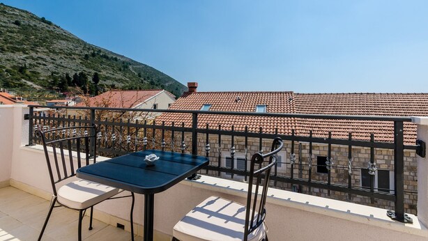 A balcony with a table and chairs, overlooking a hillside with terracotta-roofed buildings. - Apartments Life - One Bedroom Apartment with Balcony and Sea View (Dubrovnik)