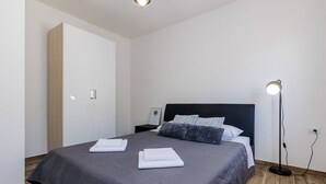 A neatly made bed with a dark grey bedspread and two neatly folded white towels. There is a black floor lamp on the right side of the bed. - Apartments Life - One Bedroom Apartment with Balcony and Sea View (Dubrovnik)