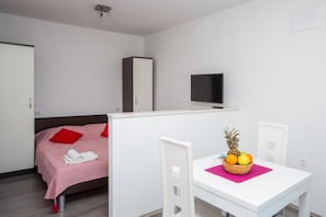 A bedroom with a bed, a TV, a wardrobe, and a dining area with a table and chairs. - Villa Roza - Studio Apartment with Balcony (Mokosica)