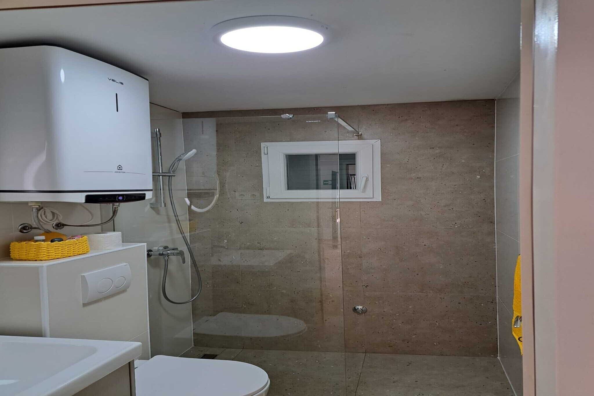 A bathroom with a toilet, a sink, a shower enclosure, and a ceiling-mounted air conditioning unit.