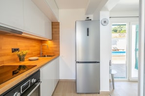 Una cucina moderna con elettrodomestici in acciaio inossidabile, un piano di lavoro in legno e vista su una piscina attraverso una porta aperta.