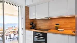 Une cuisine moderne avec des meubles blancs, un plan de travail en bois, un four encastré et une vue sur le balcon.