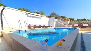 Une piscine avec des chaises longues, un mur de pierre et un ciel bleu azur.