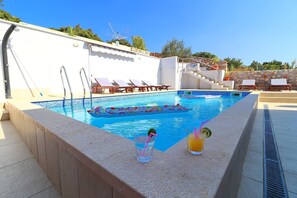 Ein Swimmingpool mit Liegestühlen, einer Steinmauer und einem wolkenlosen, blauen Himmel.