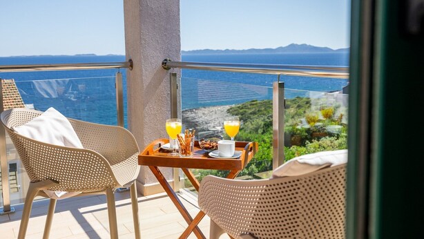 Un balcon avec une table préparée pour le petit-déjeuner, offrant une vue sur un paysage côtier.