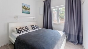 Ein Schlafzimmer mit Bett, einem Fenster mit Vorhängen, einem Bild an der Wand und einer Deckenleuchte.