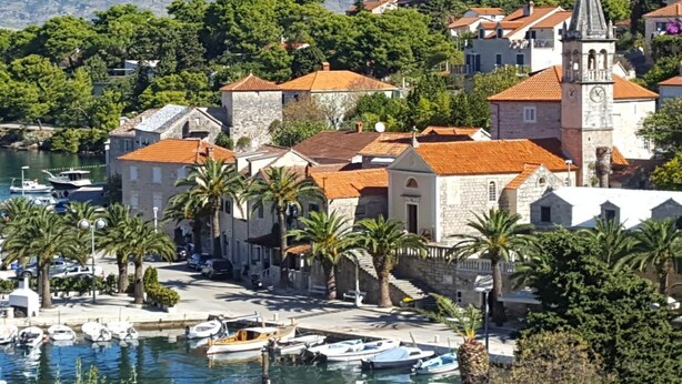 Une ville côtière avec des bâtiments en pierre, un clocher d’église imposant et un port de plaisance rempli de bateaux.