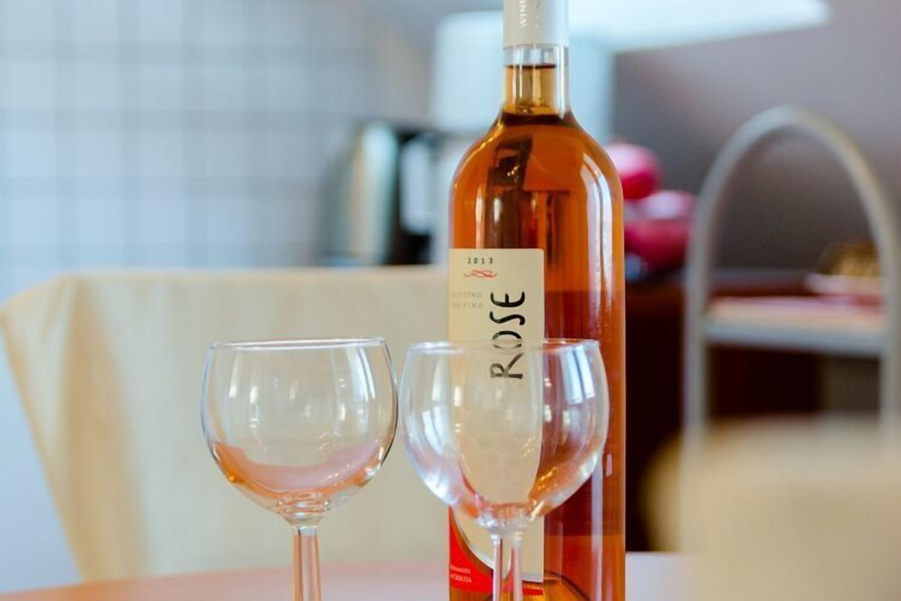 A bottle of Rose wine and two empty wine glasses on a table.