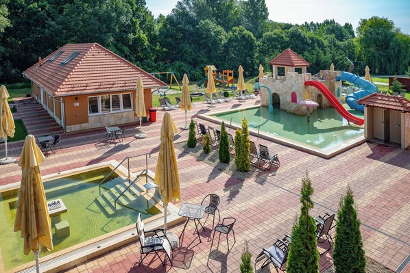 A pool area with a slide, lounge chairs, and a small building. - Termál Hotel Vesta (Tápiószecso)
