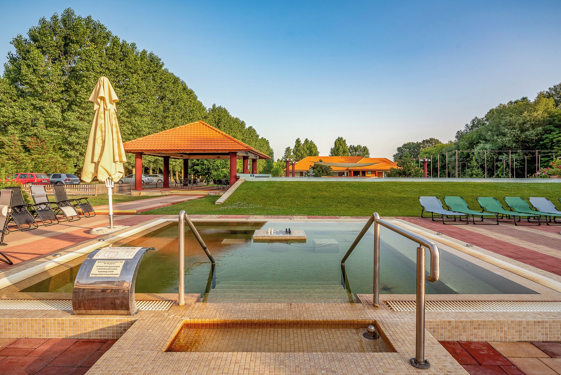 A swimming pool with a sunbathing area, lounge chairs, and a pavilion.