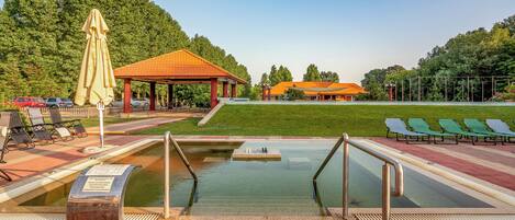A swimming pool with a sunbathing area, lounge chairs, and a pavilion.