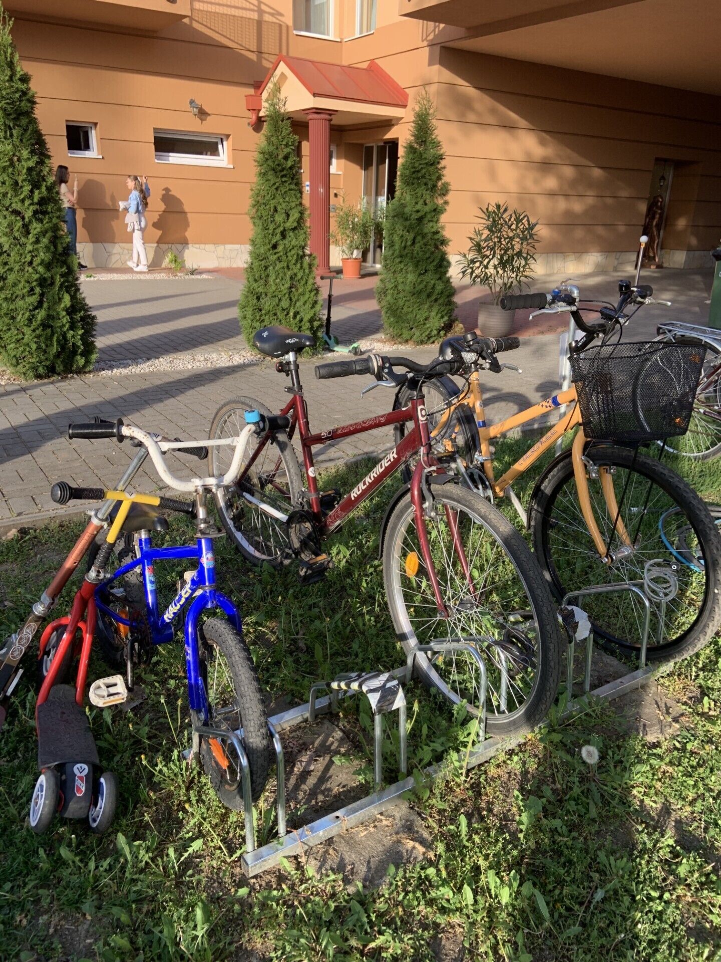 A row of bicycles parked on a rack in front of a building with a red roof and a window.