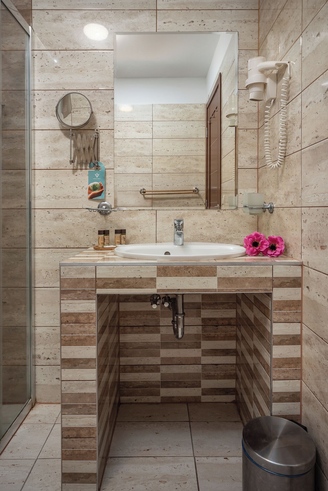 Un baño con lavamanos, espejo, toallero y un cubo de basura.