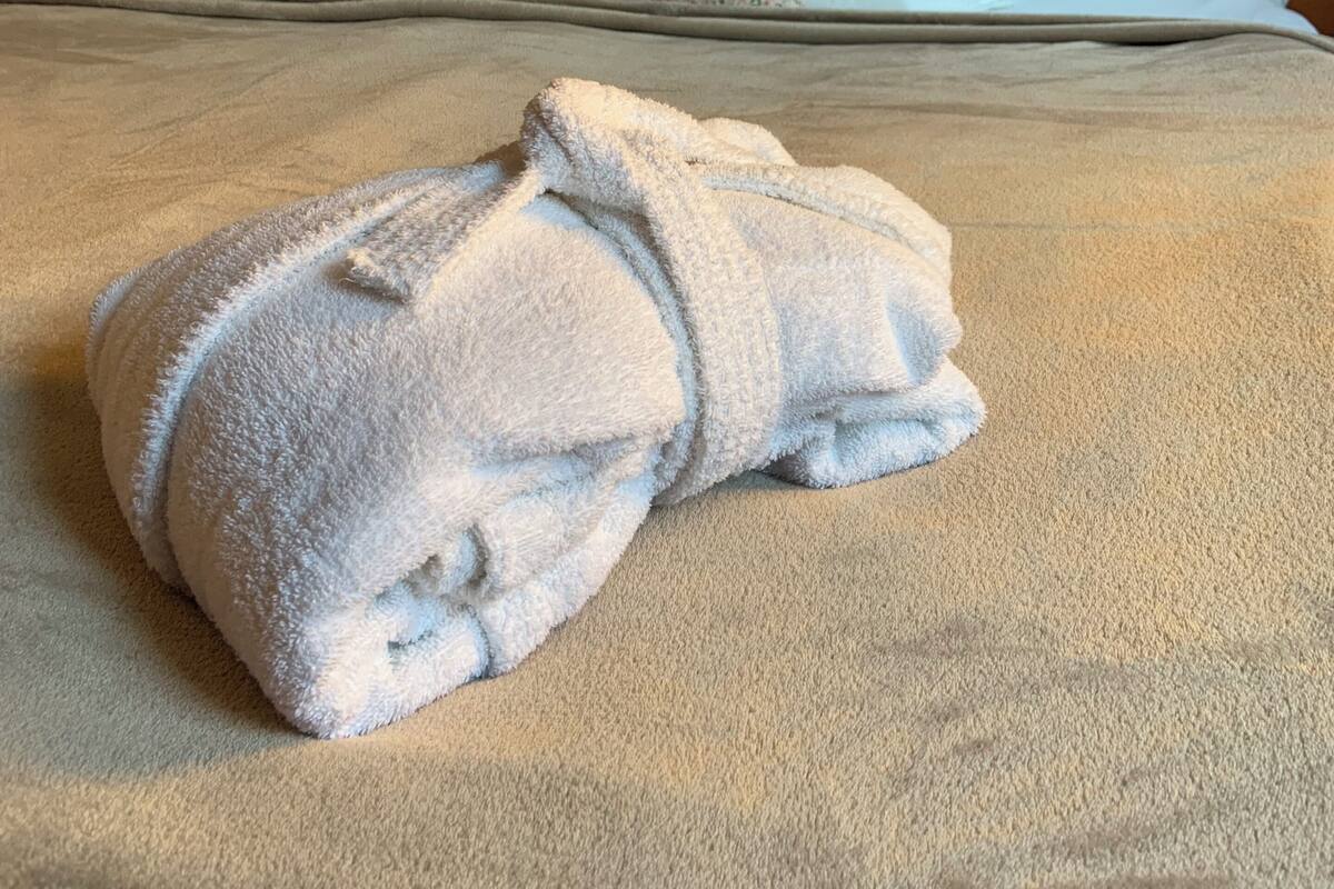 Una cama bien hecha con una toalla doblada, un cojín floral y un cabecero con textura.