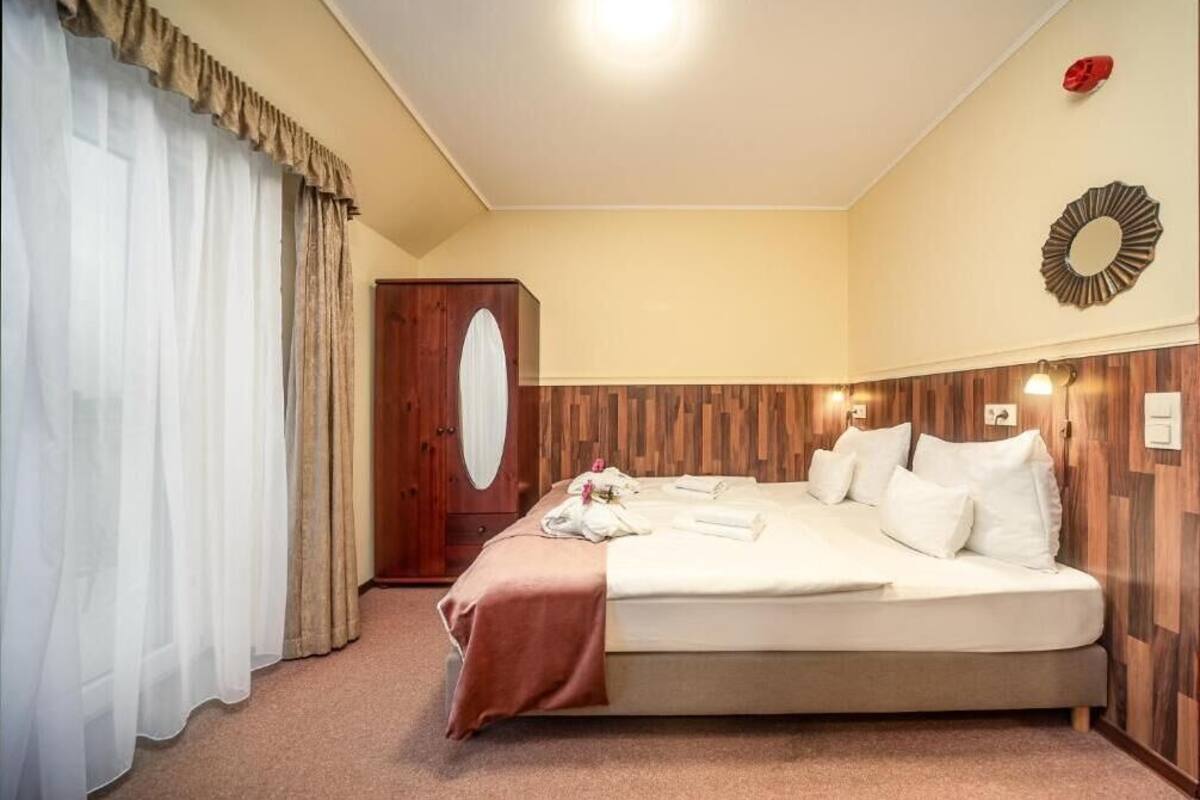 Una habitación de hotel con cama, cortinas, un armario de madera y luces fijadas a la pared.