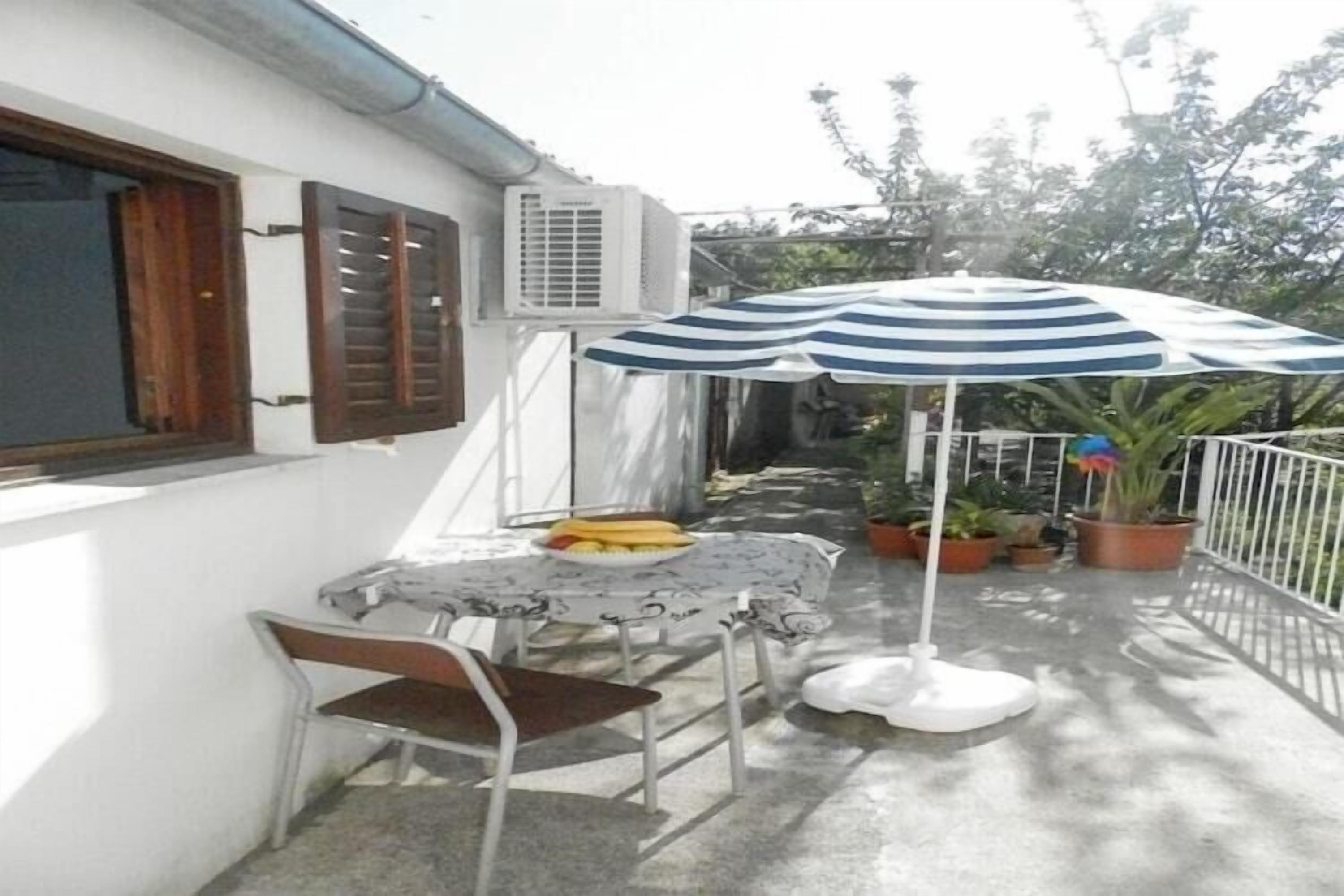 Une terrasse avec une table, des chaises, un parasol à rayures, des plantes en pot et un appareil de climatisation.