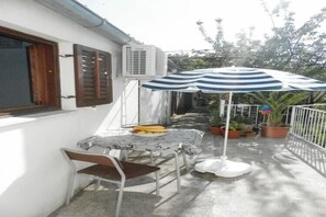 Une terrasse avec une table, des chaises, un parasol à rayures, des plantes en pot et un appareil de climatisation.