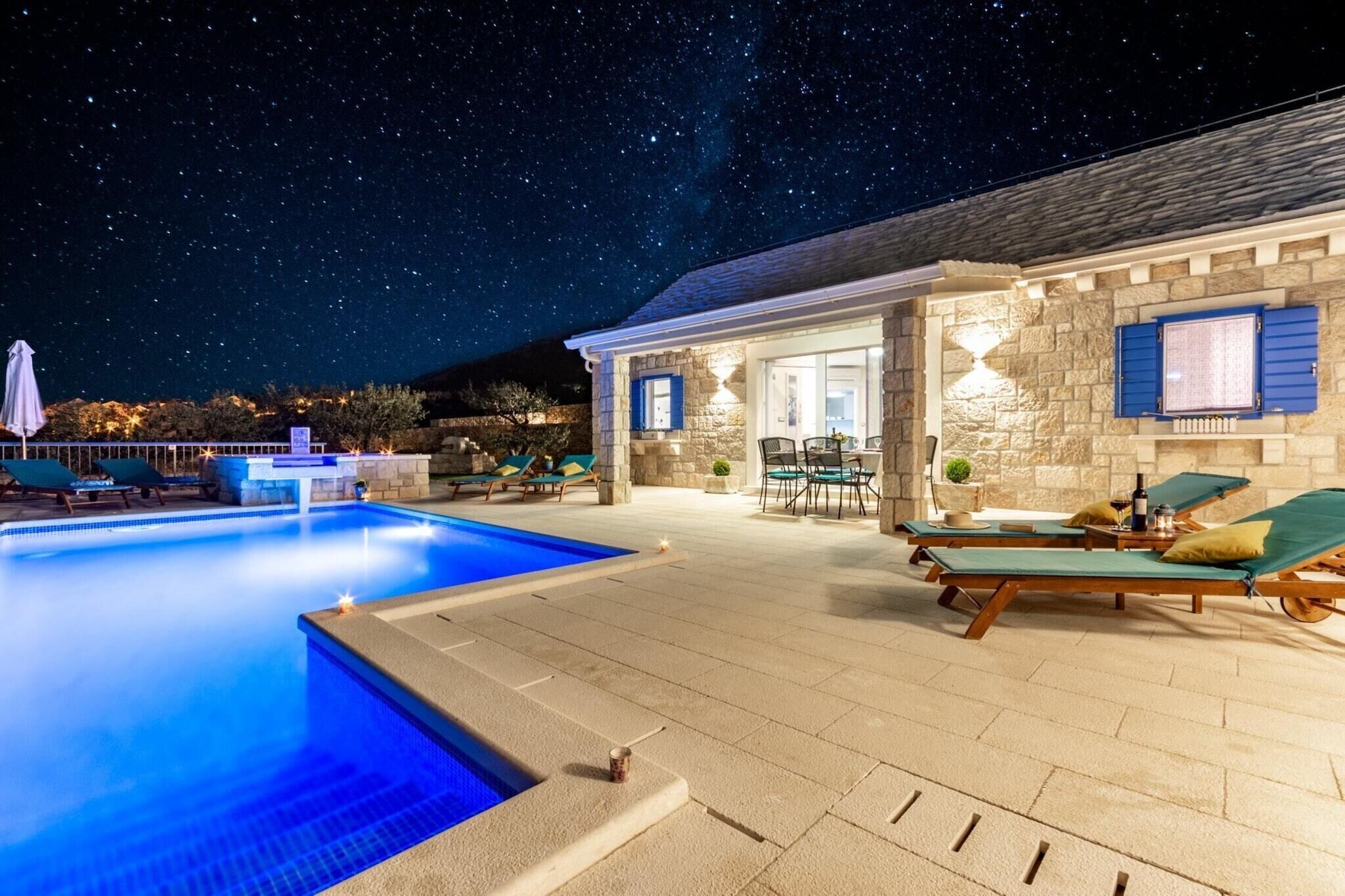 A poolside area with a stone building, outdoor seating, and a night sky.