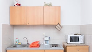 Una cocina compacta con armarios de madera, un fregadero, un microondas y una cafetera.