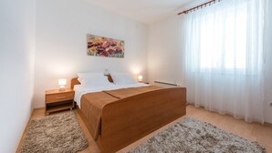 A bedroom with a wooden bed, white bedding, a nightstand with a lamp, a fluffy rug, and a painting on the wall.