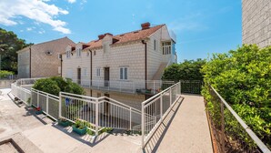 A two-story building with a tiled roof, a balcony, and a fenced courtyard with potted plants.