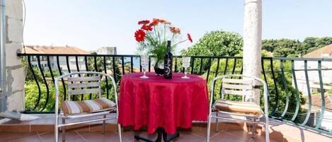 Un balcon avec une table rouge, deux chaises et un vase de fleurs.