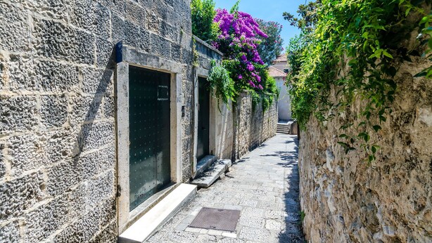 A narrow stone pathway flanked by buildings with steps leading up to a door.